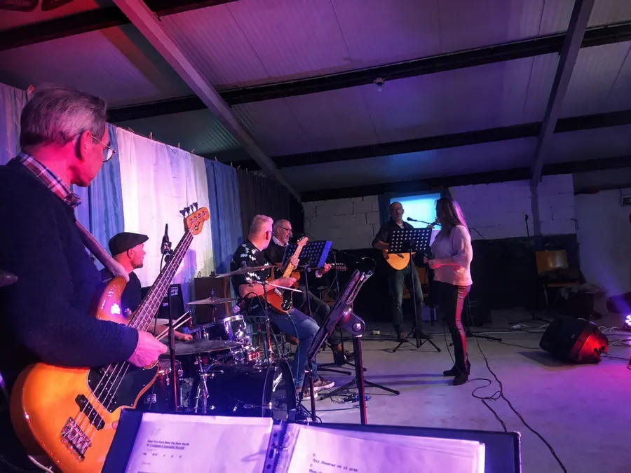 Vanaf de zijkant van het podium gezien: de bassist op de voorgrond, daarachter de drummer, twee gitaristen en de zangeres bij de microfoon.